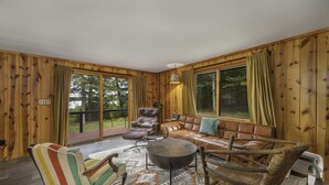 Una habitación acogedora con paredes de madera, un sofá, un sillón a rayas, una mesa redonda y una silla de mimbre.