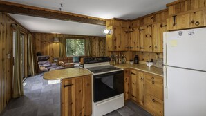 Cocina de cabaña de madera con estufa, refrigerador y armarios de madera.