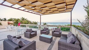 An outdoor patio with wicker furniture, a glass table, and a view of the ocean. - Villa Akumal, A Peaceful Space for 6 with Private Jacuzzi *  Steps to the Beach! (Akumal)