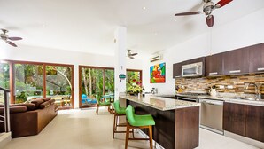 A modern kitchen with a central island, bar stools, and a view of a pool and outdoor area. - Villa Akumal, A Peaceful Space for 6 with Private Jacuzzi *  Steps to the Beach! (Akumal)