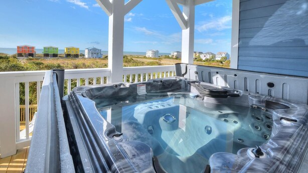 Un jacuzzi en una terraza cubierta con vista al océano y casas al fondo.