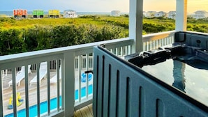 Un balcón con hidromasaje, piscina y vistas a casas coloridas y la playa.