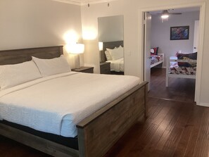 Un dormitorio con cama de madera, lámparas de noche, un espejo y una puerta que da a otra habitación.