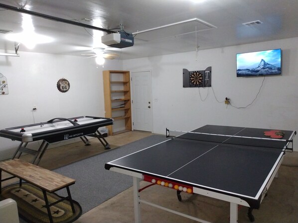 Una habitación con mesa de ping pong, mesa de fútbol de mesa, dardos y una televisión montada en la pared.