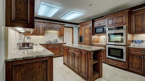 Une cuisine dotée de meubles en bois, de plans de travail en granit et d’appareils électroménagers intégrés, notamment un four à micro-ondes, un four et une cuisinière.