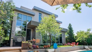 Una casa moderna de dos pisos con piscina, mobiliario exterior y plantas en macetas.