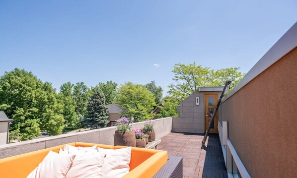 A rooftop terrace with a wooden deck, a yellow sofa, and potted plants.