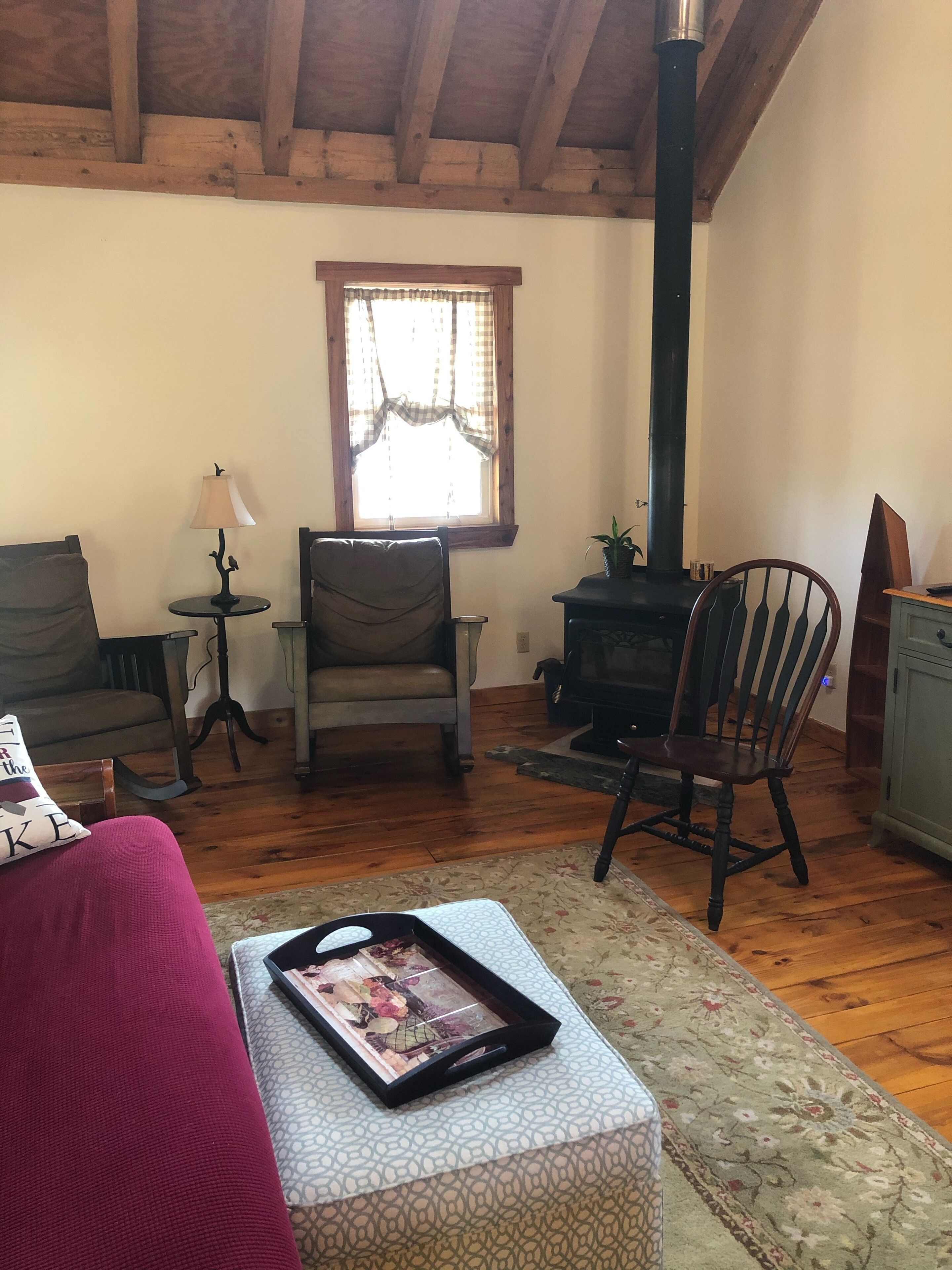 Un salon chaleureux avec un plafond en bois, une cheminée, un canapé, un fauteuil et une petite table avec une lampe.