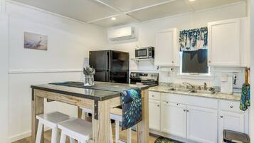 A compact kitchen with white cabinets, a refrigerator, microwave, and a peacock-themed tablecloth.