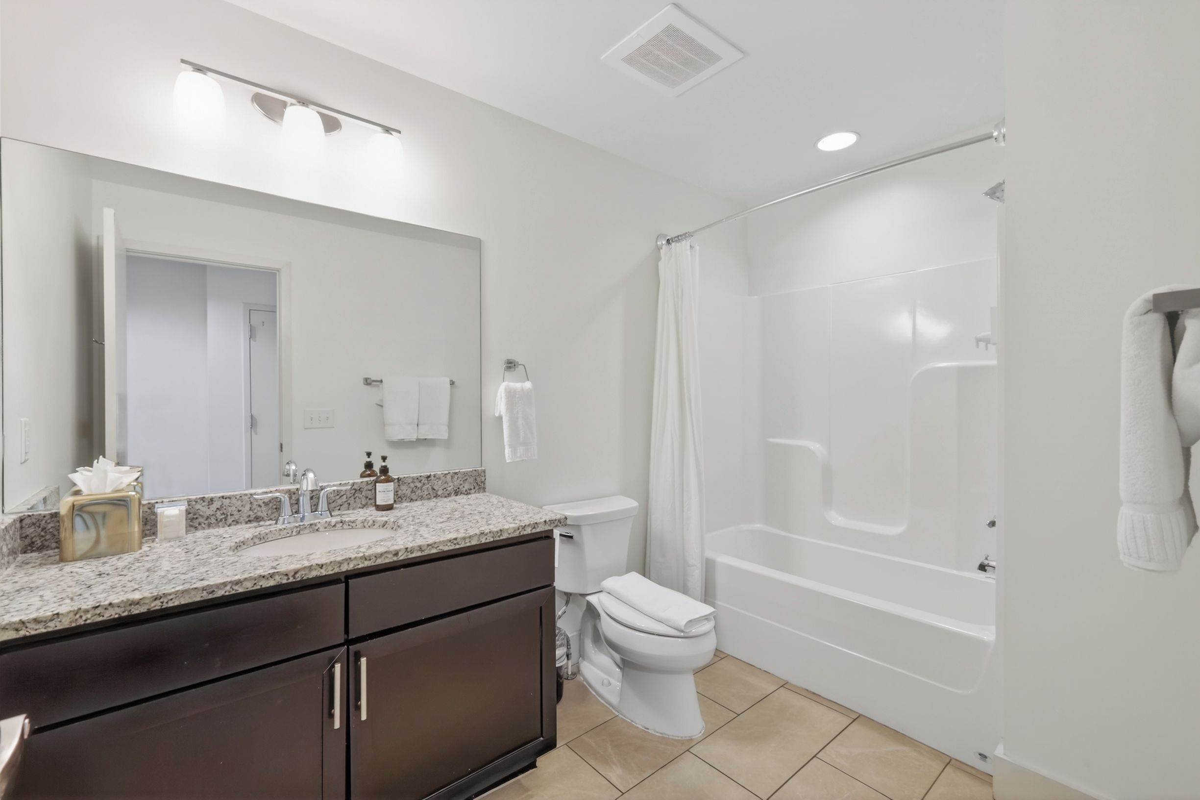 A modern bathroom with a large mirror, a sink with a marble countertop, a toilet, and a walk-in shower.