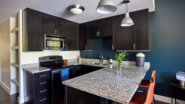 A modern kitchen with dark cabinets, a granite countertop, a central island with seating, and pendant lighting.