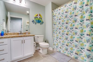 Un baño con inodoro, lavamanos y cortina de ducha con motivos marinos.