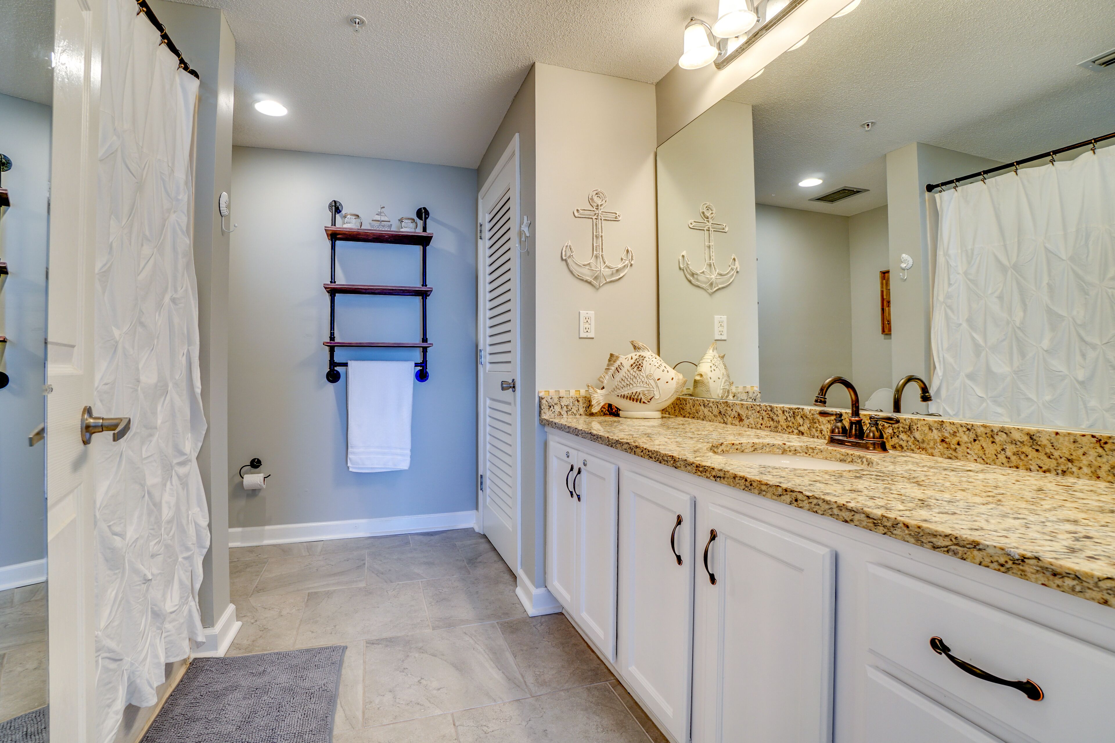 A bathroom with a white vanity, a sink with a granite countertop, a large mirror, and a towel rack.