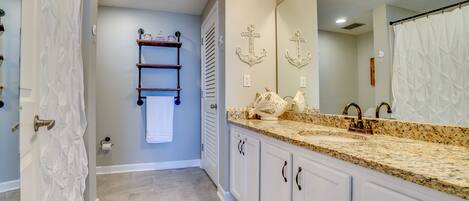 A bathroom with a white vanity, a sink with a granite countertop, a large mirror, and a towel rack.
