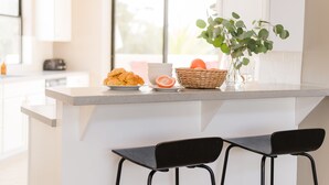 A kitchen counter with a basket of bread, a bowl of fruit, and a potted plant. - Ivory I By AvantStay | Modern Home w/ Stunning Views | Close To Old Town (Scottsdale)