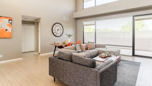 A modern living room with a gray sectional sofa, a dining table with chairs, a large wall clock, and a sliding glass door leading to a balcony. - Ivory I By AvantStay | Modern Home w/ Stunning Views | Close To Old Town (Scottsdale)