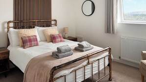 Une chambre à coucher avec un lit, une table de chevet, une lampe, un miroir et une fenêtre avec des rideaux.