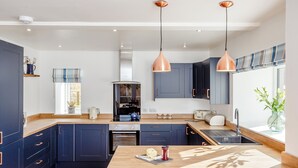 Une cuisine moderne avec des meubles de couleur bleu foncé, un plan de travail en bois et des suspensions lumineuses en cuivre.