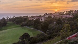 Ein Golfplatz mit Blick auf eine Küstenstadt und den Ozean bei Sonnenuntergang.