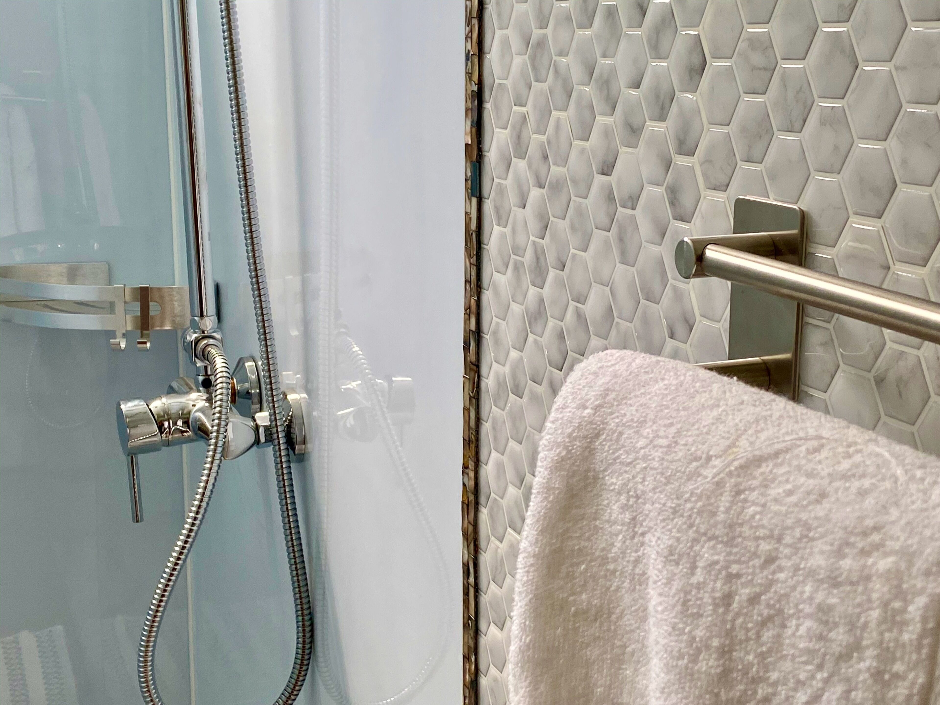 A bathroom with a glass shower door, a towel rack, and a hexagonal tiled wall.
