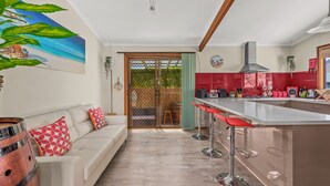 Une cuisine moderne avec un coin bar, un canapé blanc agrémenté de coussins rouges et une grande fenêtre donnant sur un jardin.