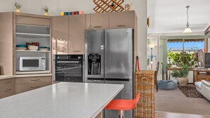 Une cuisine moderne dotée d’un grand îlot central, d’appareils électroménagers en acier inoxydable et d’un coin repas avec une chaise et un canapé en osier.