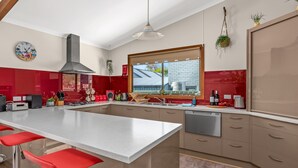 Une cuisine moderne dotée d’un grand îlot central, de tabourets de bar rouges, d’un four encastré et d’une fenêtre donnant sur l’extérieur.