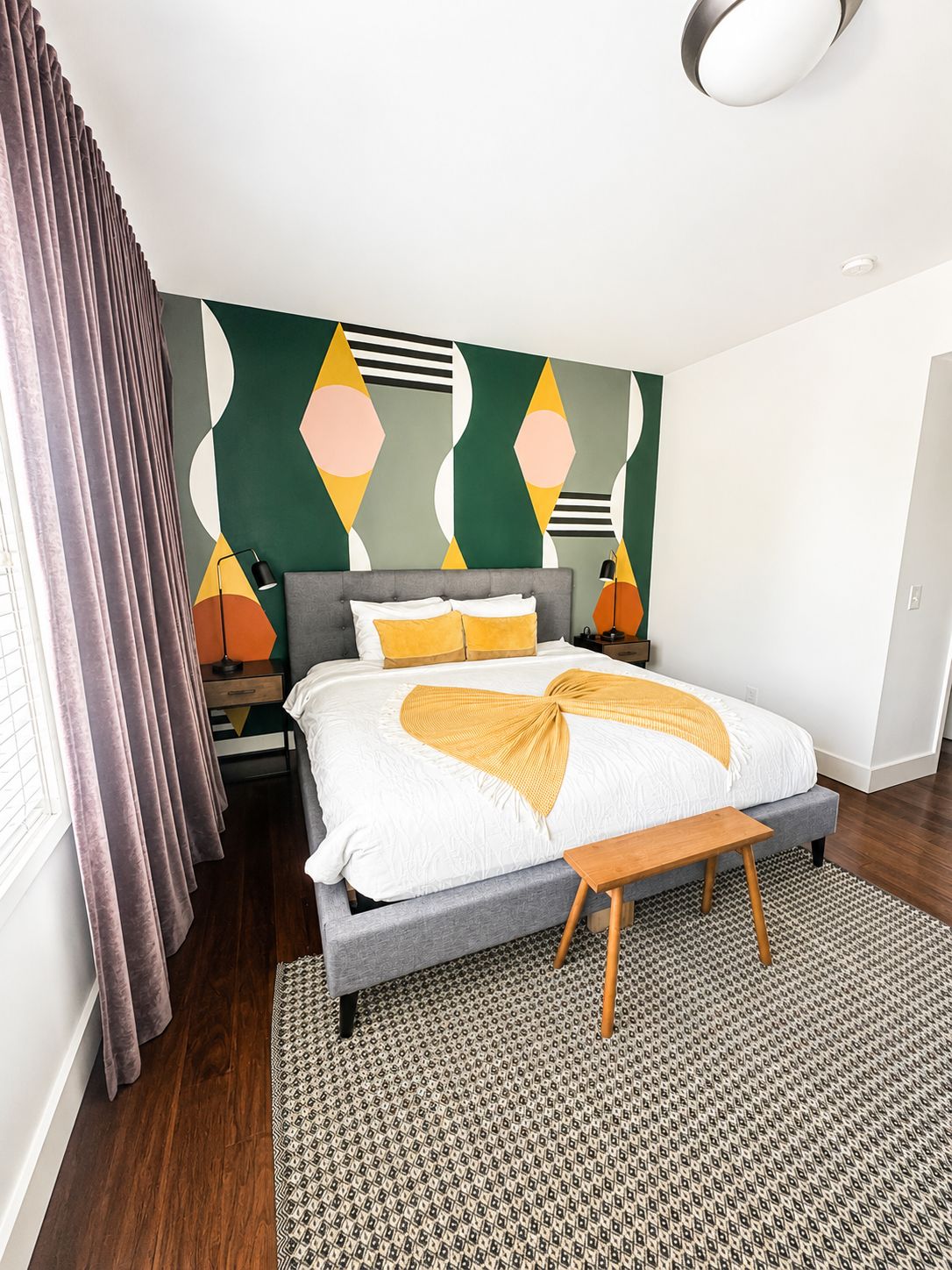 Un dormitorio moderno con una cama grande, un tapiz estampado y un mural geométrico en la pared.