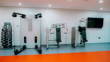 Une salle de sport équipée de divers appareils d’exercice, d’un téléviseur fixé au mur et d’un mur décoré de motifs.