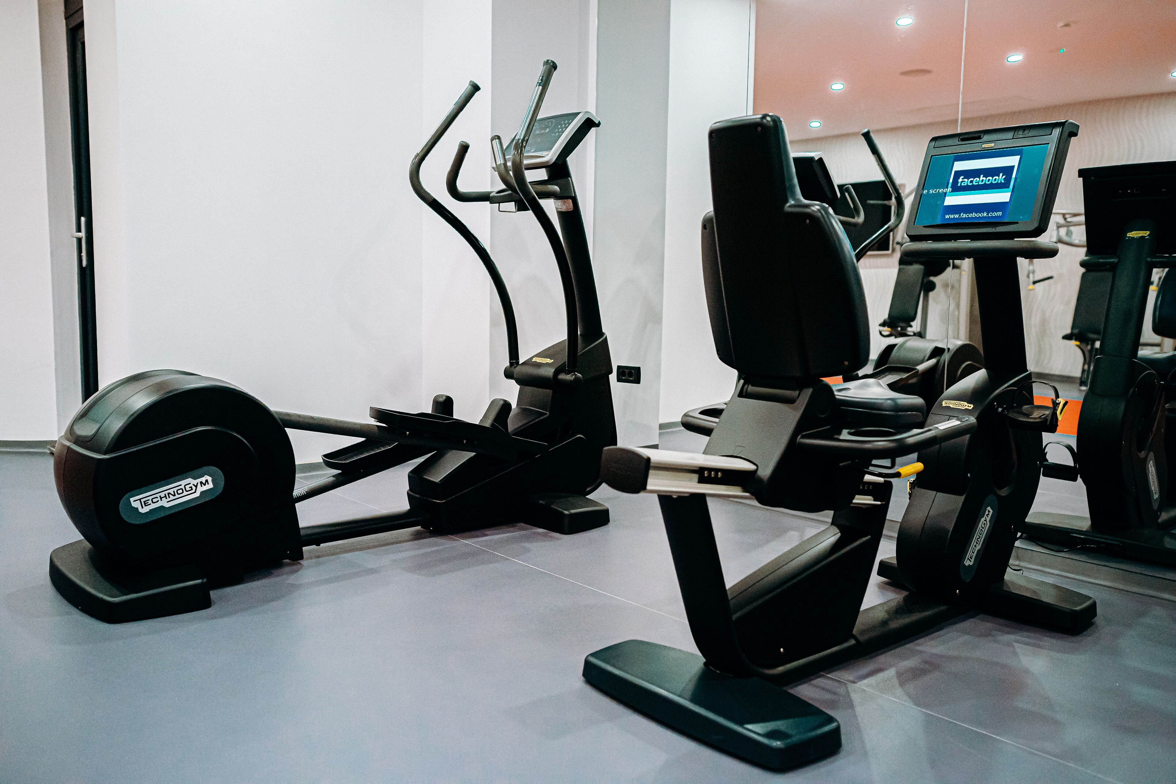 Ein Fitnessraum mit verschiedenen Trainingsgeräten, darunter Laufband, Crosstrainer und Kraftgeräte.
