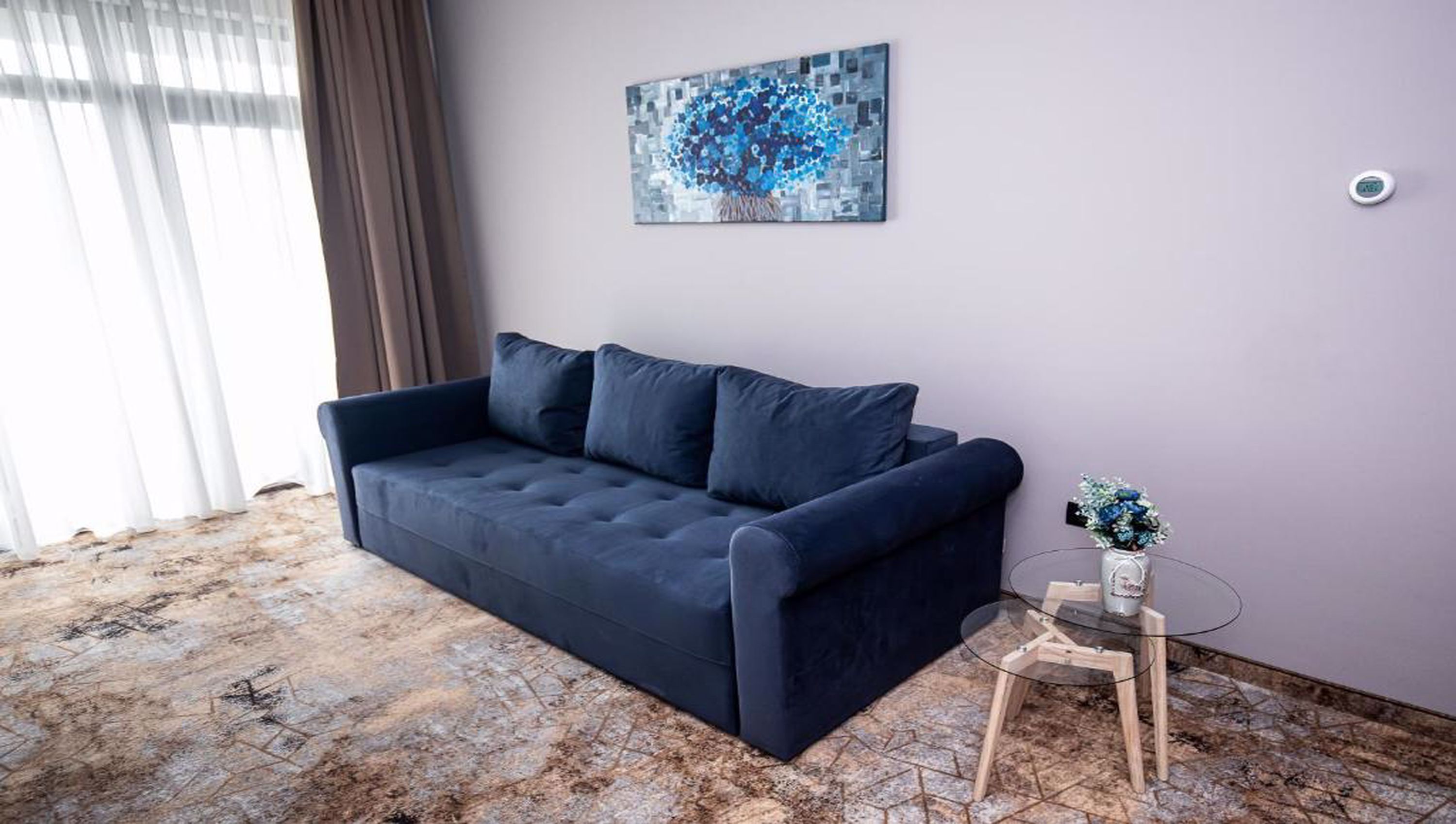 A modern living room with a dark blue sofa, a glass coffee table, and a painting on the wall.
