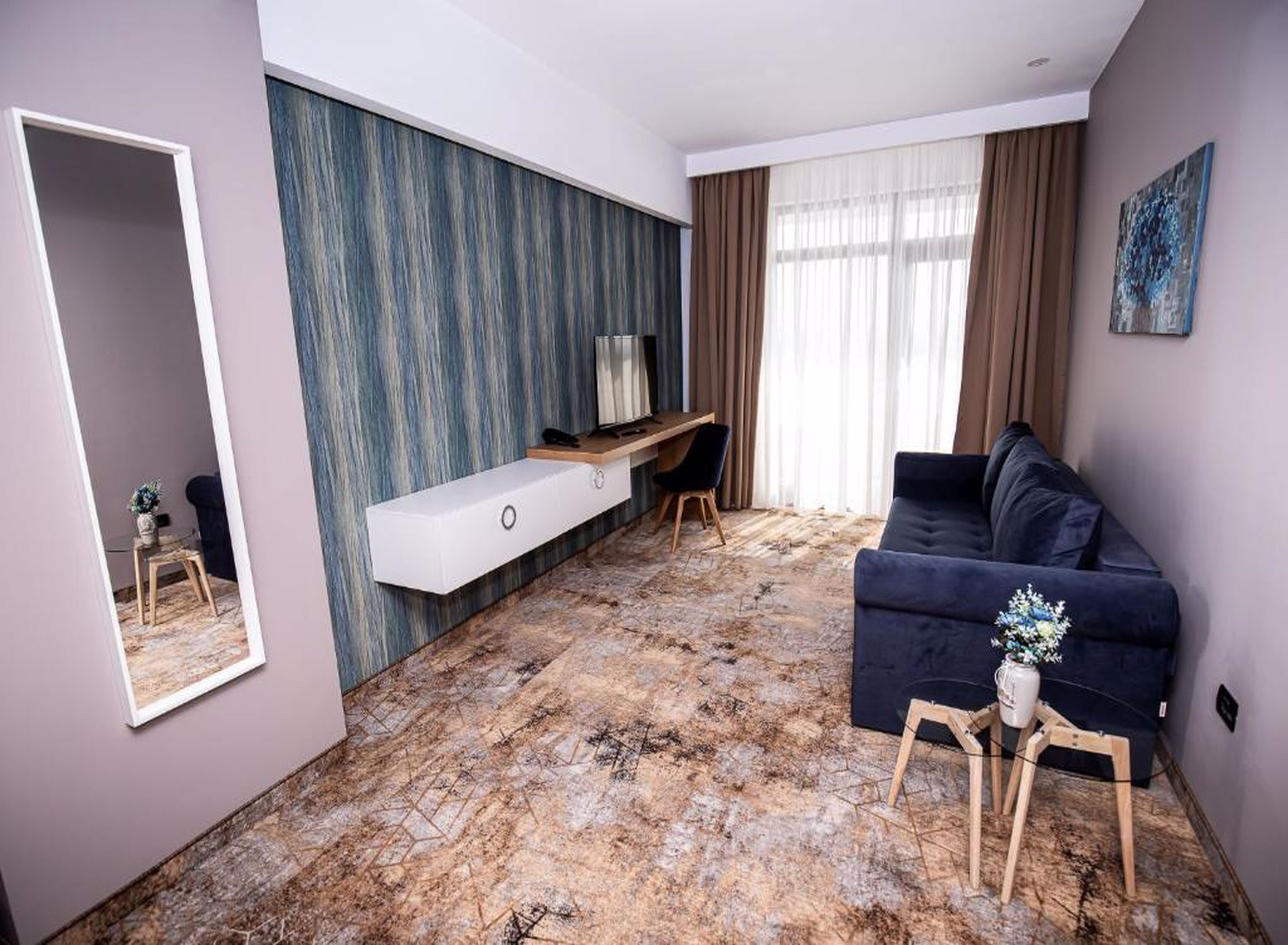 Una sala de estar moderna con un sofá azul oscuro, una consola blanca, un escritorio de madera y un espejo grande.