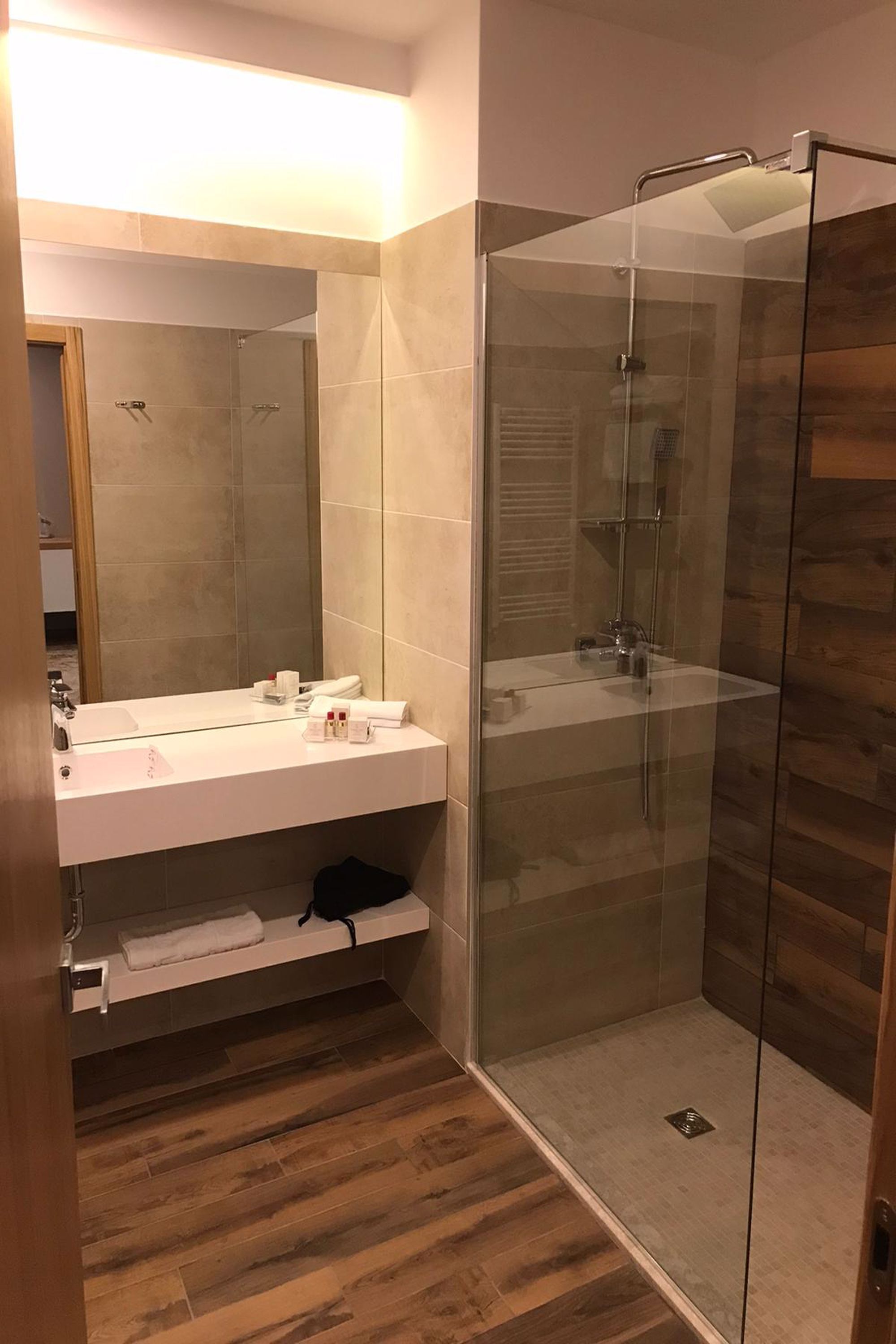 Ein modernes Badezimmer mit einer einteiligen Glasdusche, einem weißen Waschbecken mit Spiegel und Holzboden.