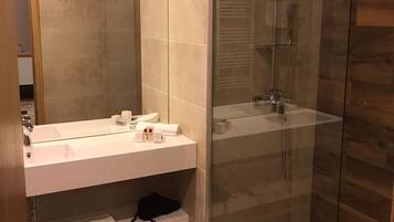 A modern bathroom with a glass-enclosed shower, a white sink with a mirror, and wooden flooring.