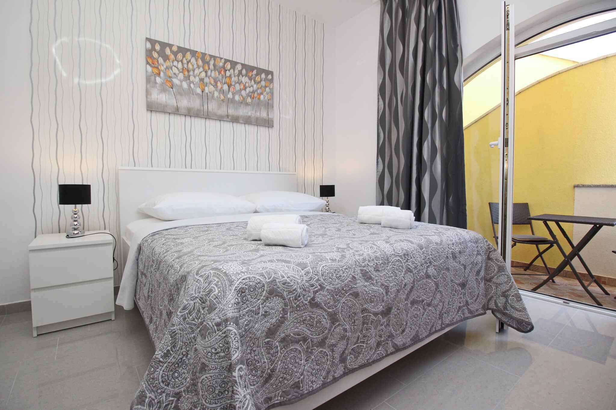 Une chambre moderne avec un grand lit, deux tables de chevet avec des lampes, une œuvre d’art murale et une vue sur l’extérieur, accessible par une porte vitrée.