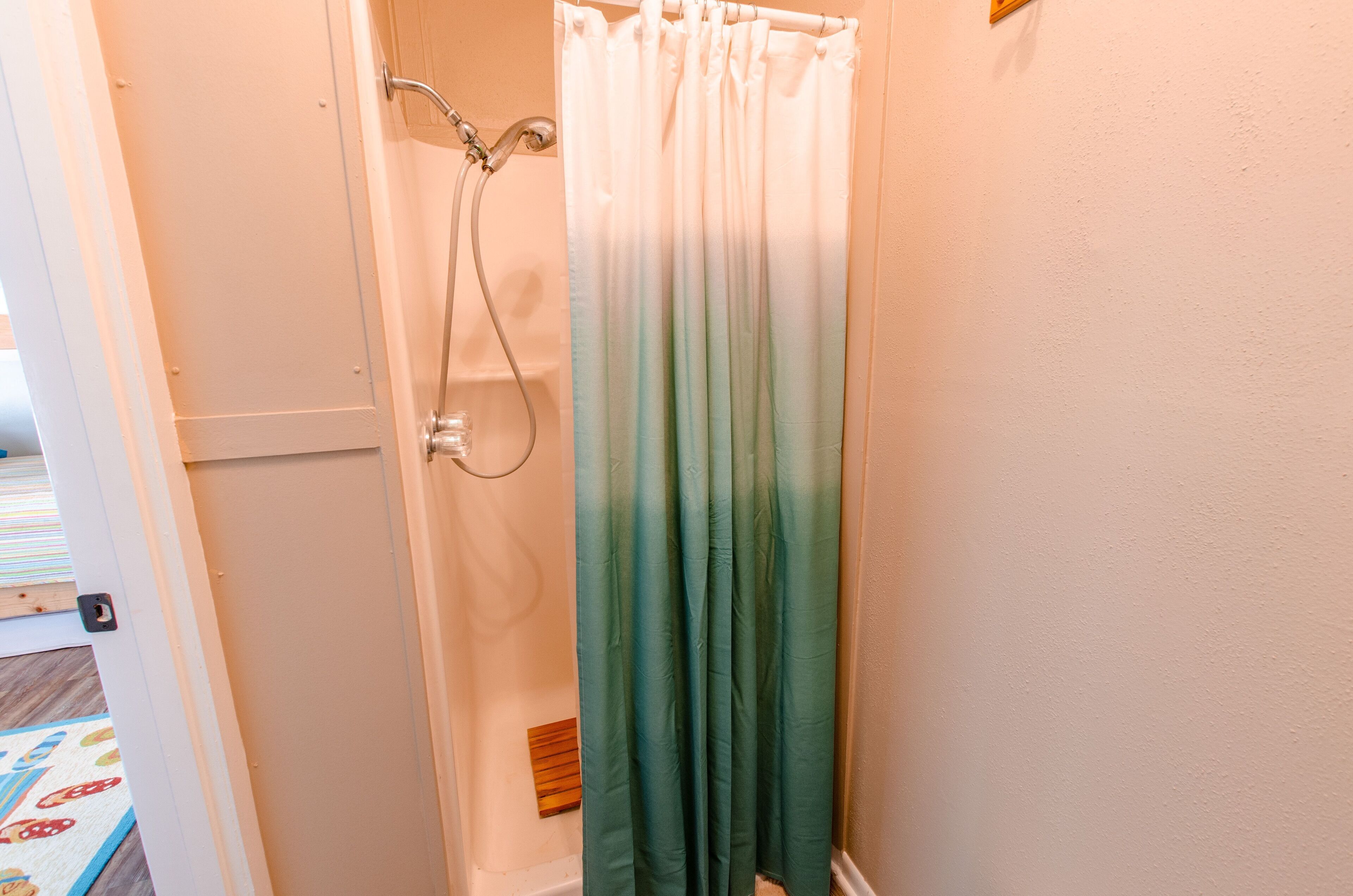 A bathroom with a shower curtain, a showerhead, and a wooden bath mat.