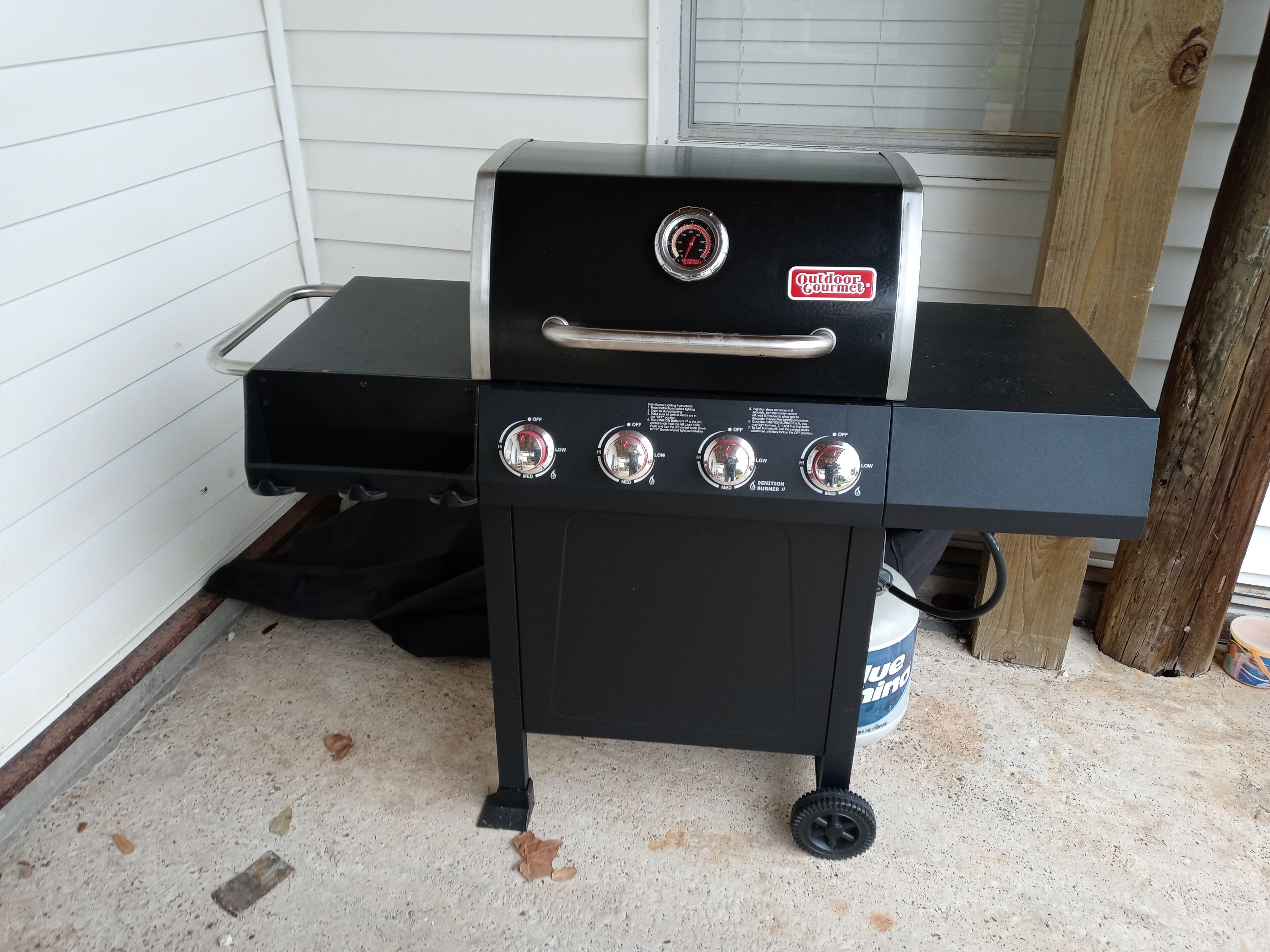 Ein tragbarer Gasgrill mit vier Brennern, einem Temperaturanzeiger und einem Griff.