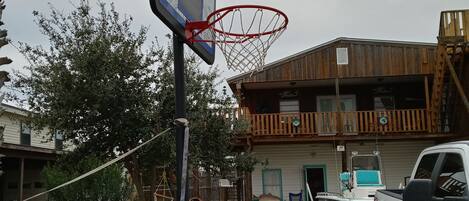 A basketball hoop in a backyard with a gravel path, a white truck, and a wooden building with a balcony.