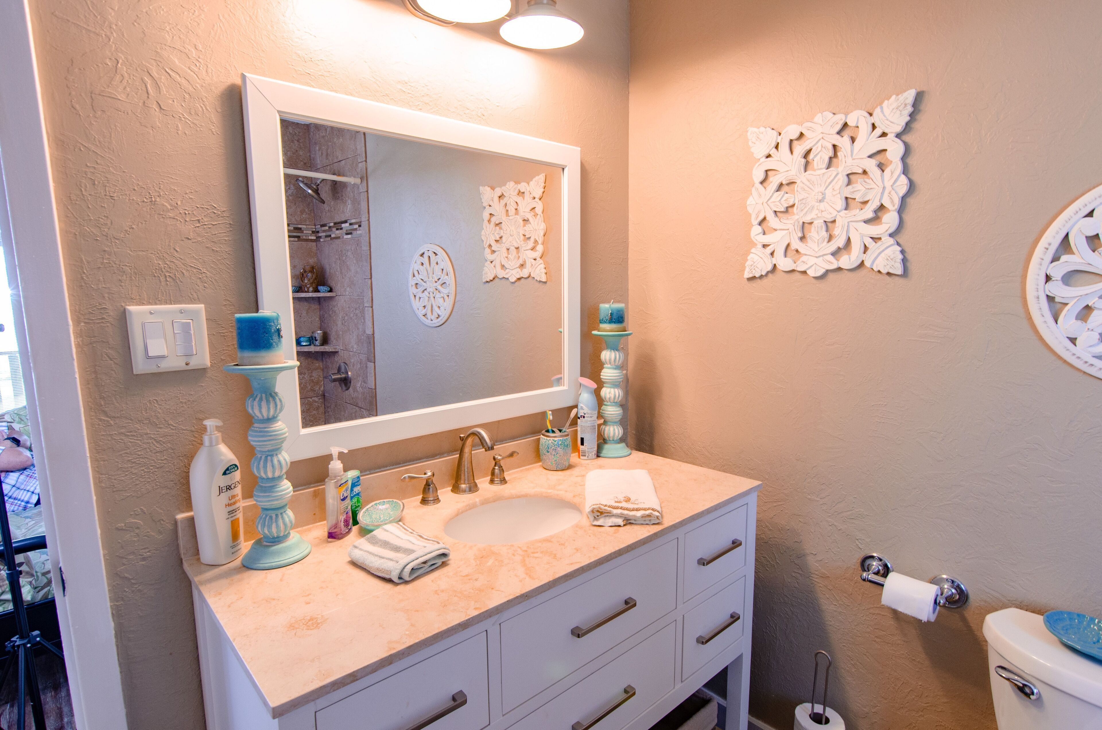 A bathroom with a sink, mirror, decorative wall pieces, and toiletries.
