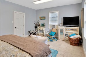 Un dormitorio con cama, televisor, cómoda, silla y ventana.