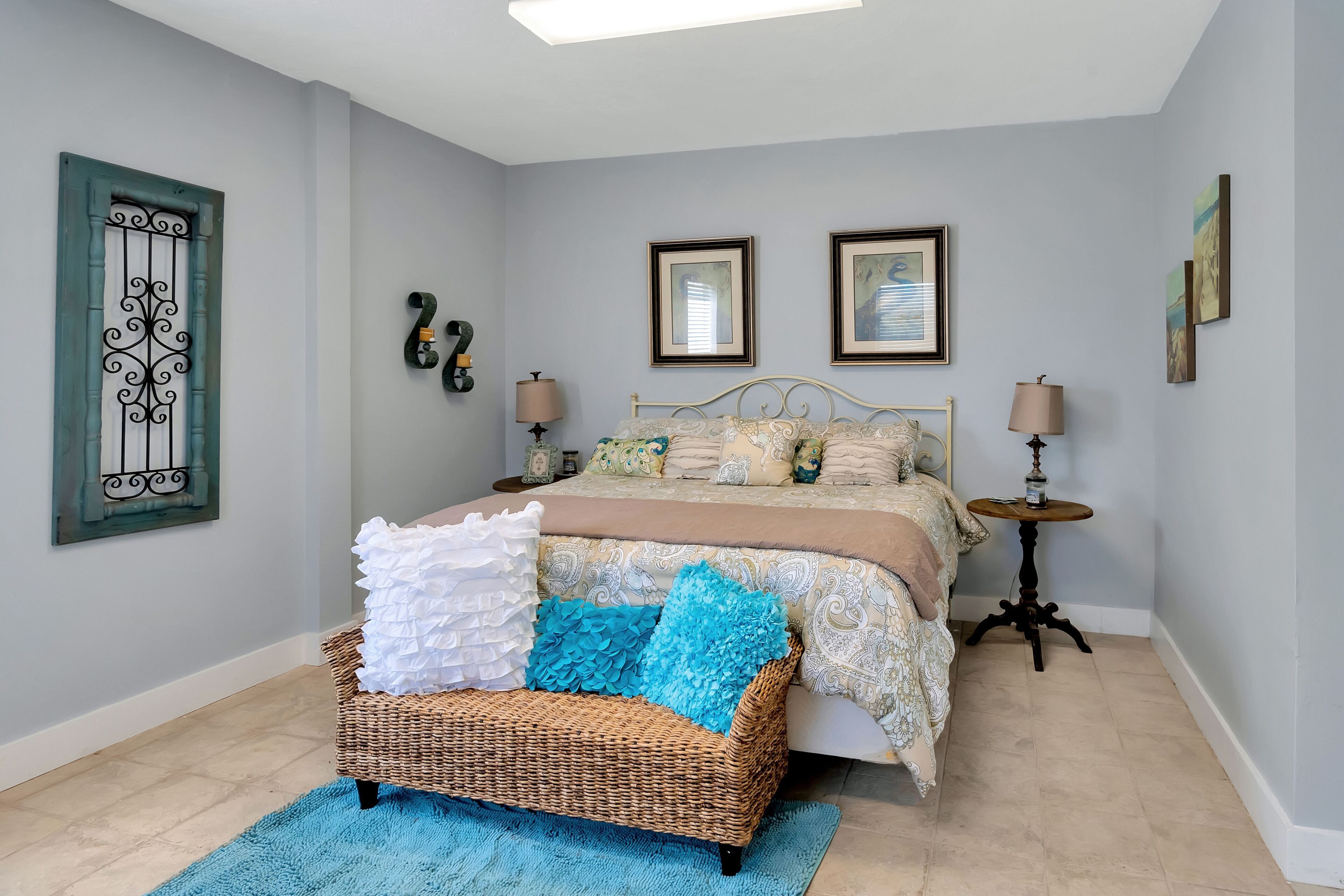 A bedroom with a bed, a wicker chair, two bedside tables, and wall decorations.