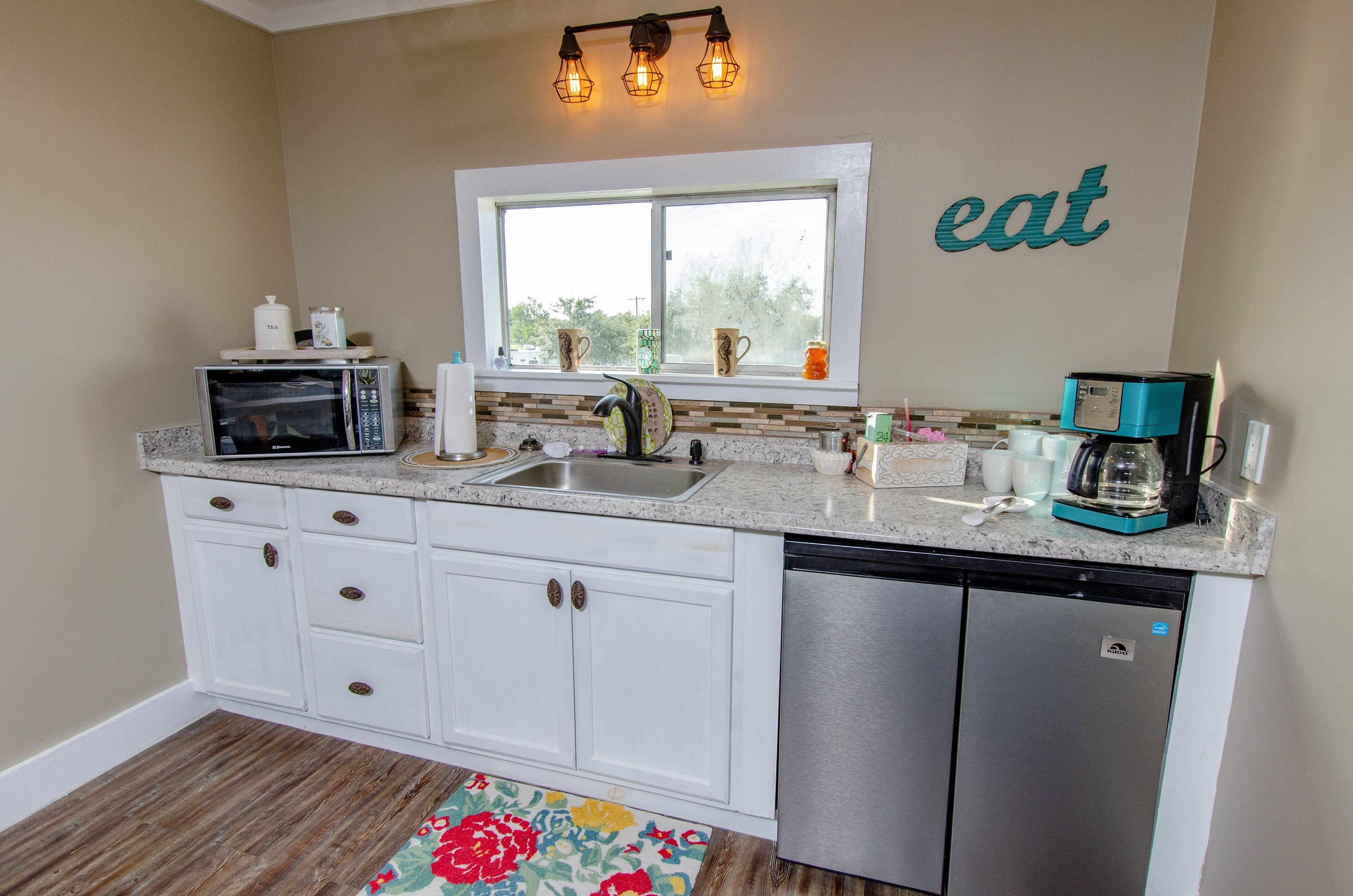 A kitchen with white cabinets, a stainless steel dishwasher, a microwave, a coffee maker, and a window with a view.