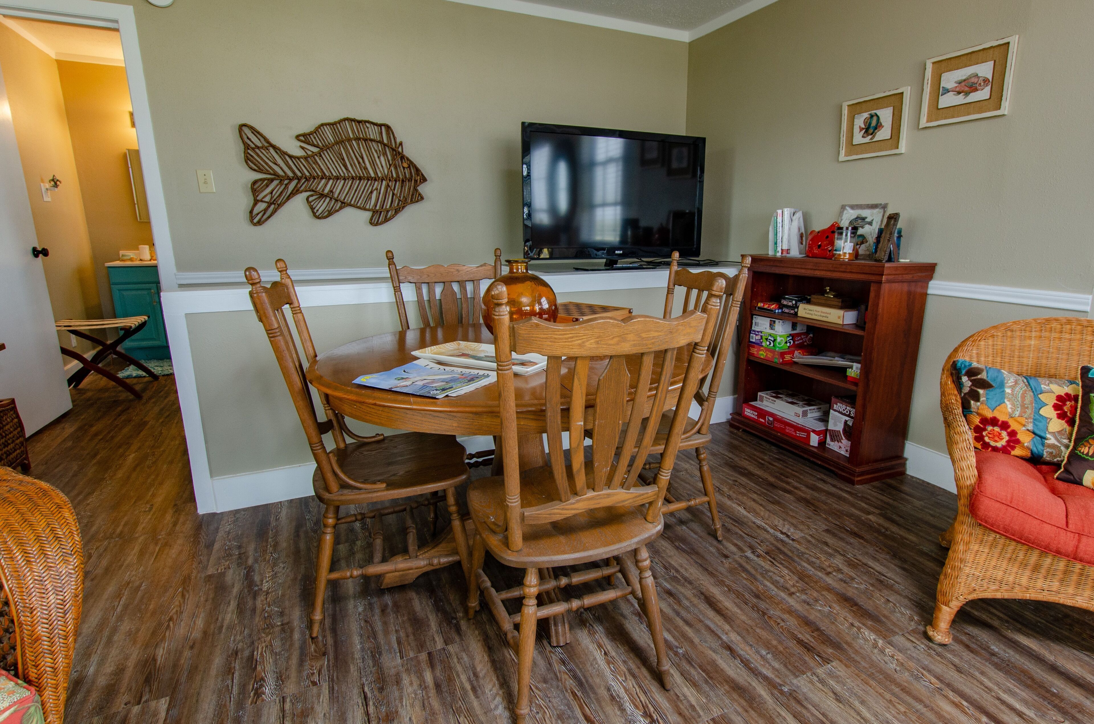 Un coin repas avec une table ronde et six chaises, un téléviseur fixé au mur et une bibliothèque contenant divers objets.
