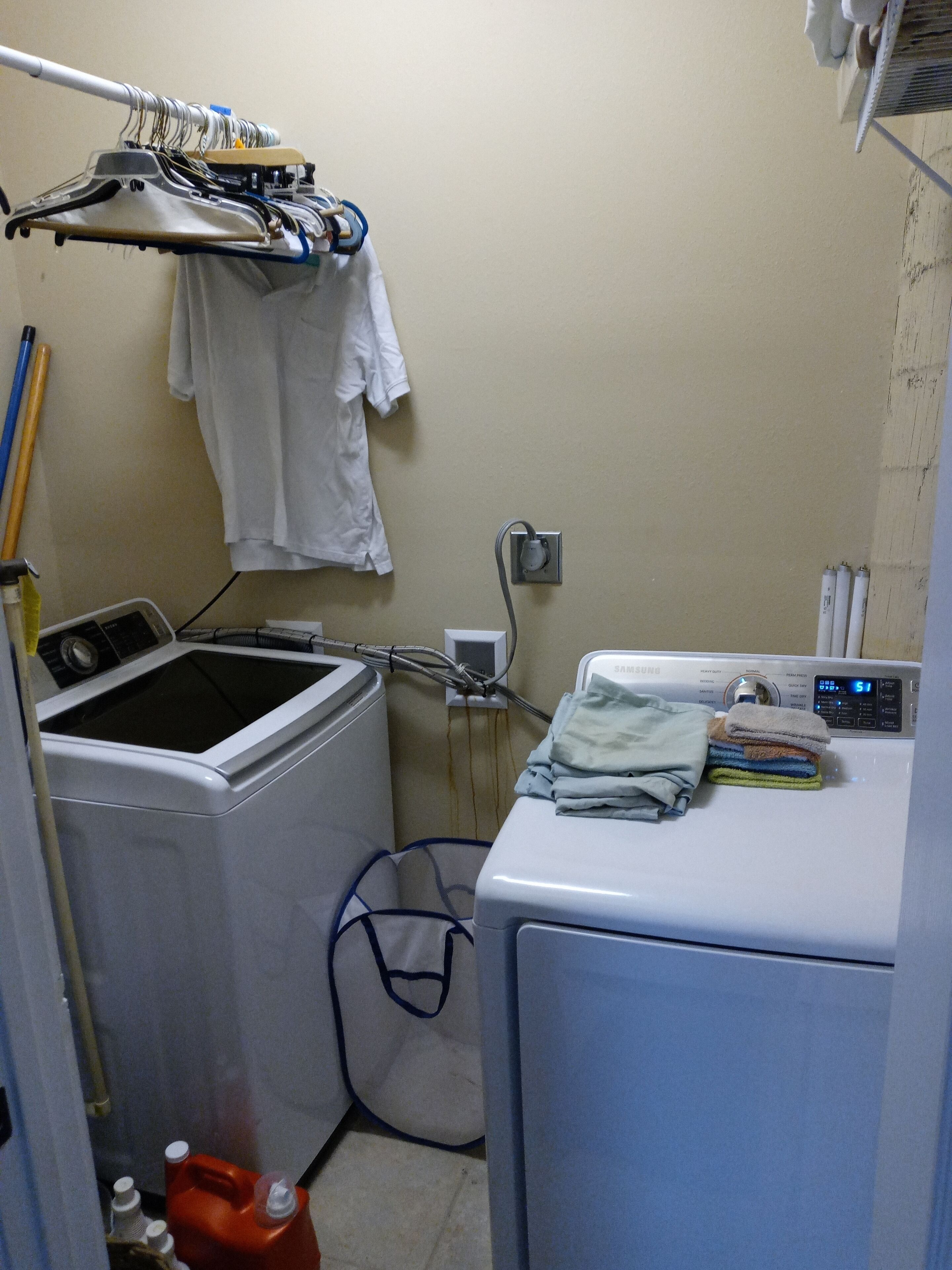 A laundry area with a front-loading washer and dryer, a drying rack, and a utility wall with a power outlet.