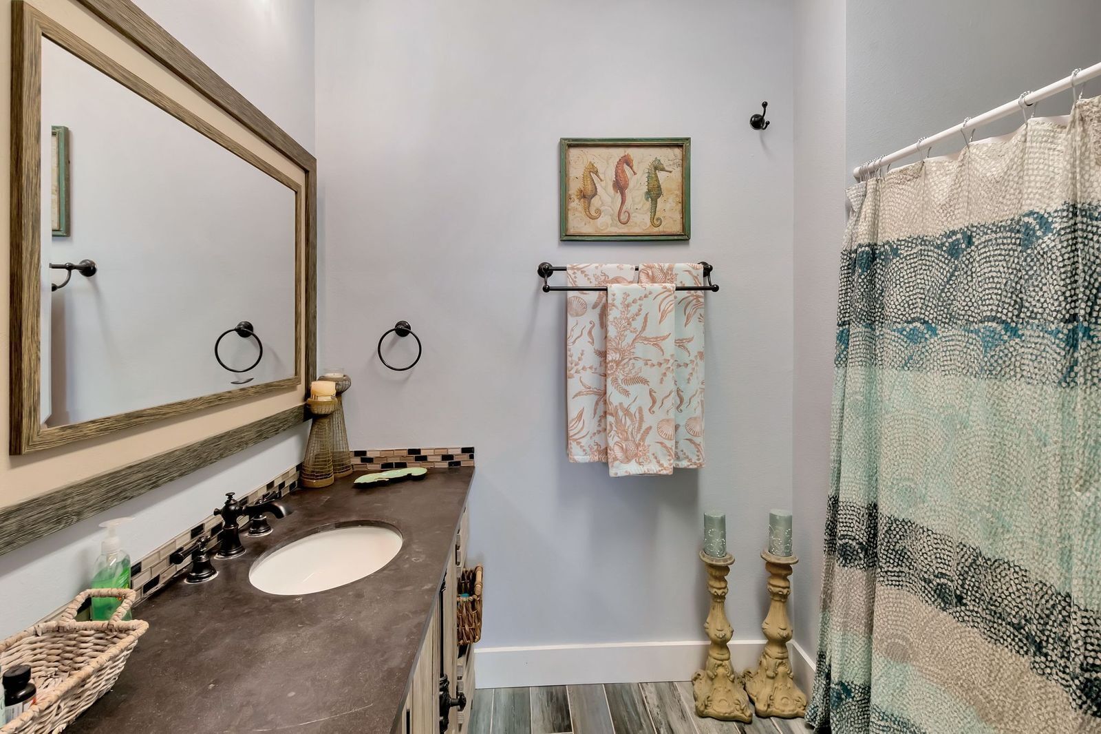 A bathroom with two sinks, a large mirror, a towel rack with a patterned towel, a decorative seahorse painting, and a patterned shower curtain.