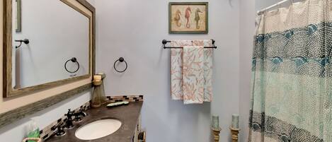 A bathroom with two sinks, a large mirror, a towel rack with a patterned towel, a decorative seahorse painting, and a patterned shower curtain.