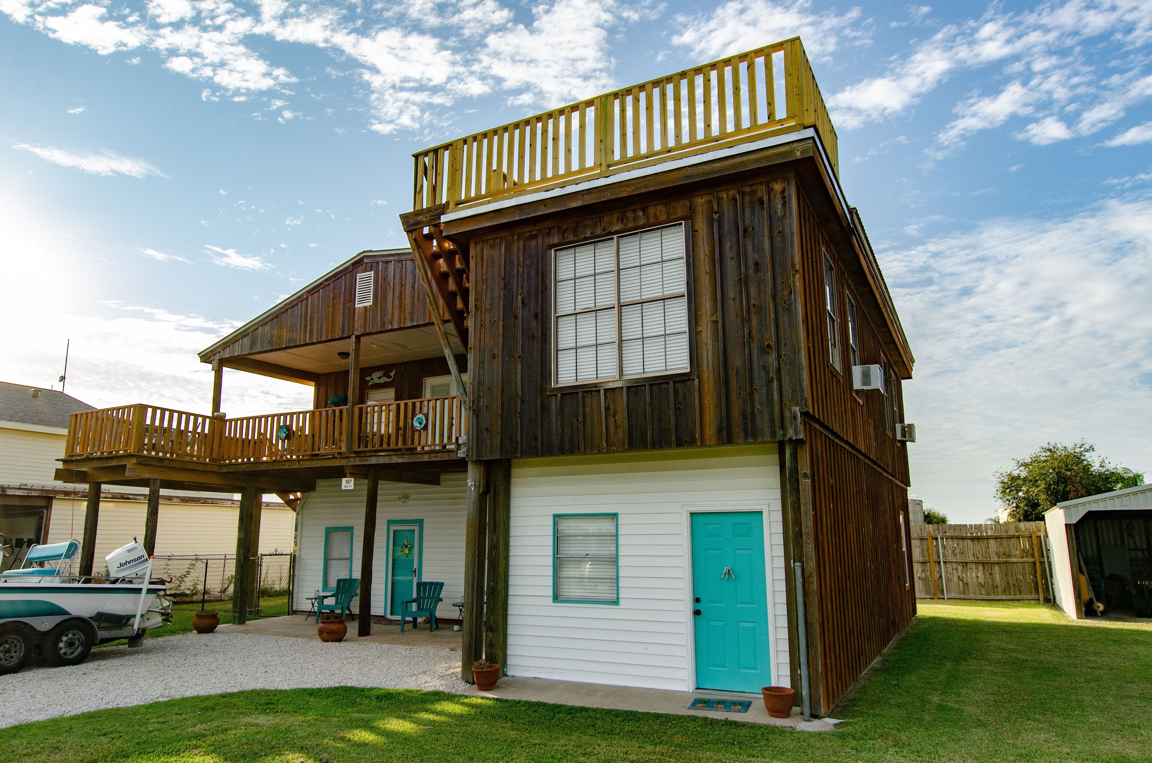 A two-story wooden house with a balcony, a garage, and a fenced yard.