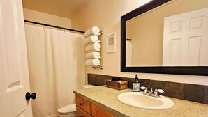 Un baño con un lavamanos blanco, armarios de madera, un espejo grande y una cortina de ducha.