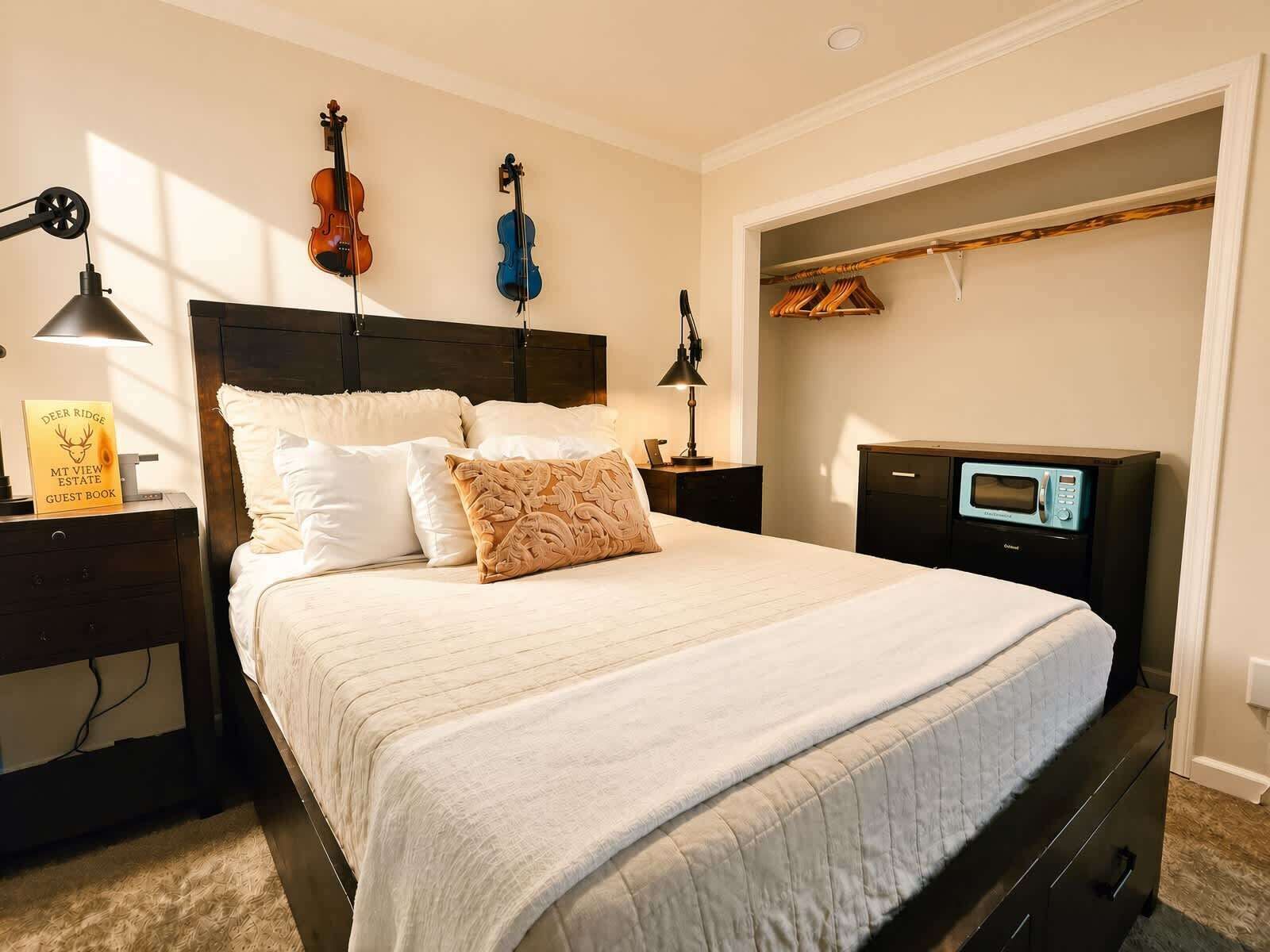 A bedroom with a bed, two bedside tables, a nightstand, a lamp, a wall-mounted TV, and a wooden closet with hanging clothes.