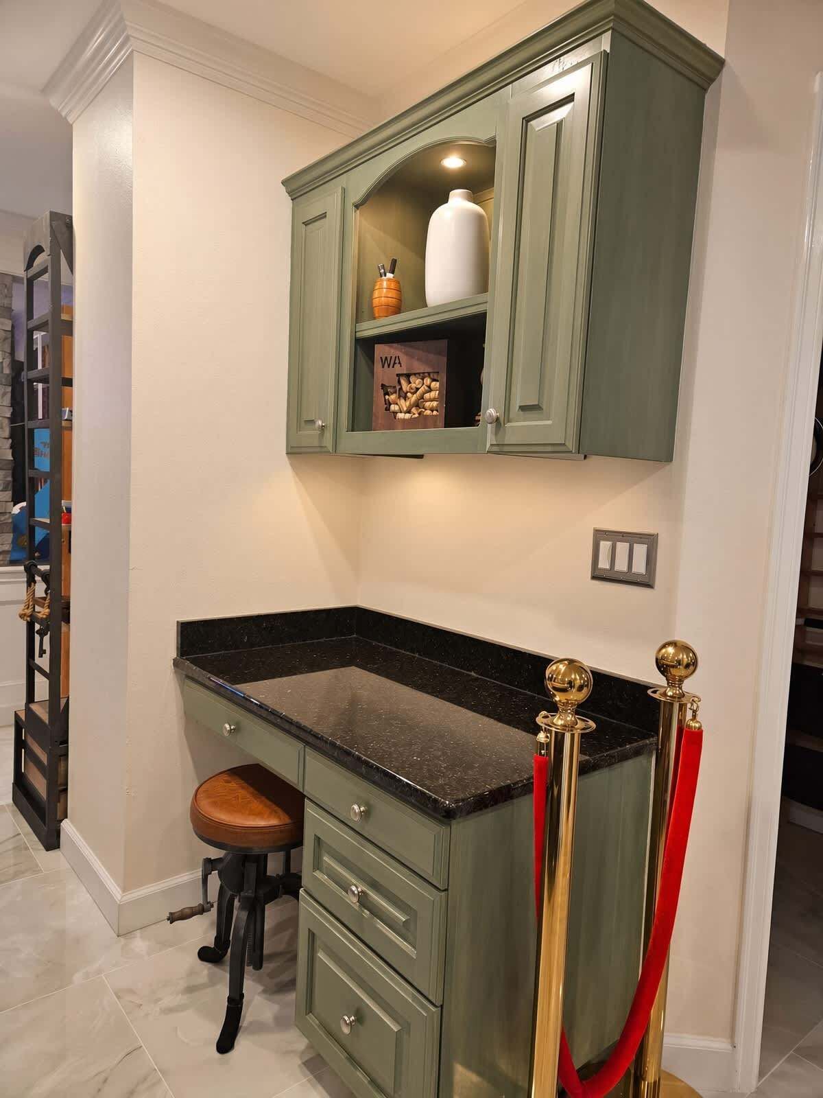 A kitchen with a green cabinet, a marble countertop, a stool, and a red rope barrier.
